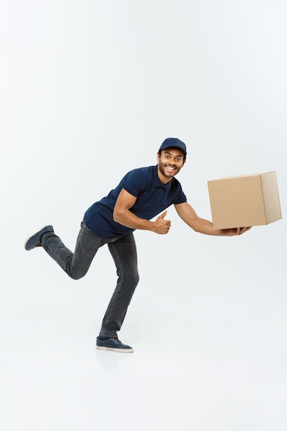 Delivery Concept - Handsome African American Delivery Man se précipite pour la livraison d&#39;un paquet pour le client. Isolé sur fond de studio gris. Espace de copie.