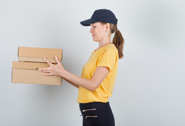 Delivery woman holding boîtes en carton en t-shirt, pantalon et casquette