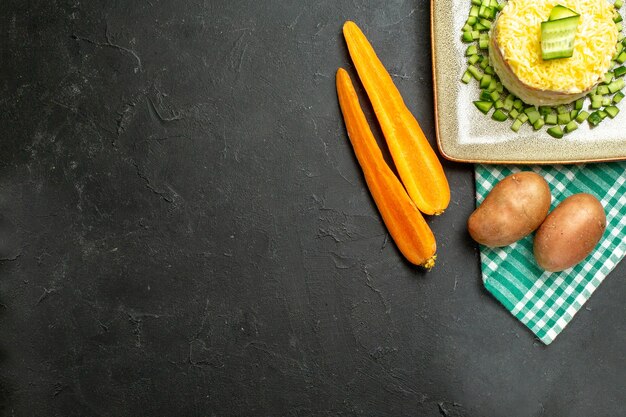 Demi-coup de délicieuse salade servie avec du concombre haché sur une serviette verte à moitié pliée et des pommes de terre carottes sur fond sombre