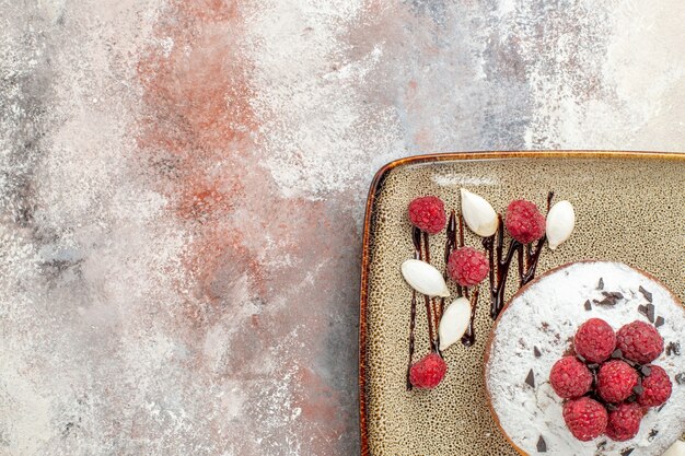 Demi-coup De Gâteau Fraîchement Sorti Du Four Avec Des Framboises Pour Les Bébés Sur Un Plateau Blanc Sur Table De Couleurs Mélangées