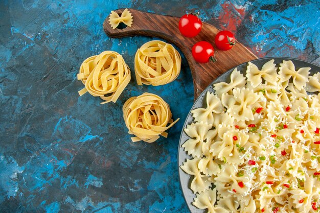 Demi-coup de pâtes farfalle aux légumes sur une plaque noire tomates sur une planche à découper en bois sur une table bleue