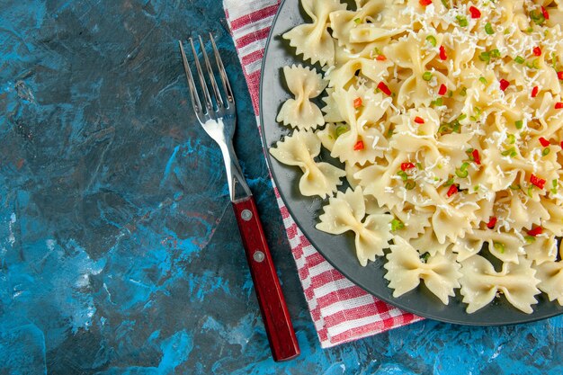 Demi-coup de pâtes farfalle italiennes crues sur une serviette à rayures rouges et des couverts sur le côté gauche sur une table bleue