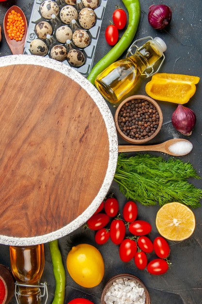 Demi-coup de planche à découper ronde parmi les légumes frais bouteille d'huile tombée au citron oeufs différentes épices sur fond noir