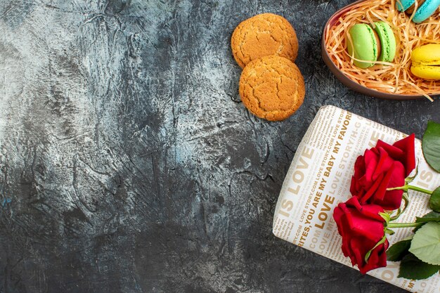 Demi-coup de rose rouge sur une belle boîte-cadeau avec de délicieux macarons et biscuits sur fond sombre glacé