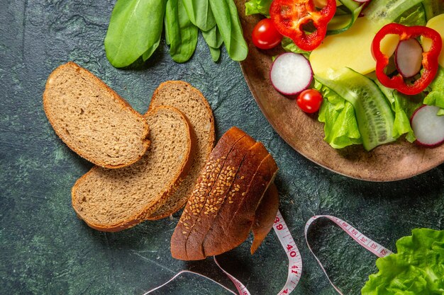 Demi-coup de tranches de pain noir de légumes frais hachés sur une assiette et des mètres de paquet vert sur la surface de couleurs foncées