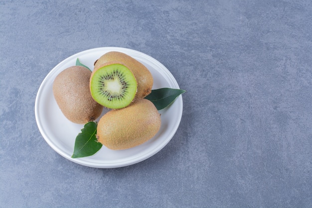 Demi-kiwis entiers sur une assiette sur la surface sombre