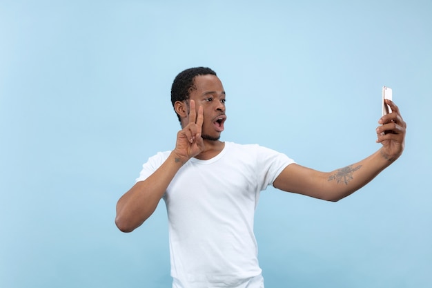 Demi-longueur gros plan portrait de jeune homme afro-américain en chemise blanche sur l'espace bleu. Émotions humaines, expression faciale, annonce, concept