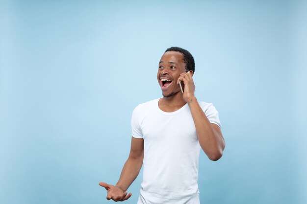 Demi-longueur gros plan portrait de jeune homme afro-américain en chemise blanche sur l'espace bleu. Émotions humaines, expression faciale, annonce, concept