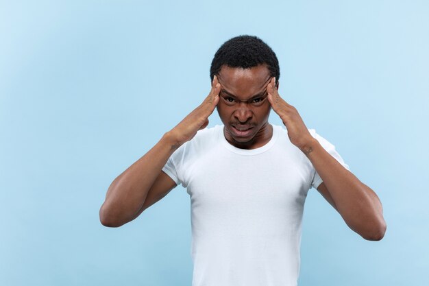 Demi-longueur gros plan portrait de jeune homme afro-américain en chemise blanche sur l'espace bleu. Émotions humaines, expression faciale, annonce, concept