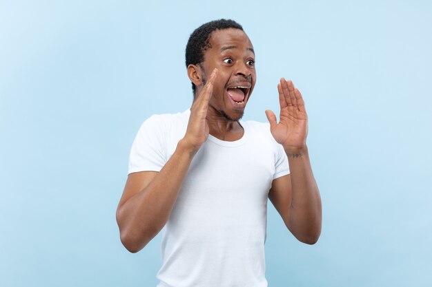 Demi-longueur gros plan portrait de jeune homme afro-américain en chemise blanche sur l'espace bleu.