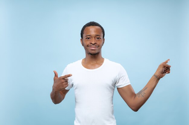Demi-longueur gros plan portrait de jeune homme afro-américain en chemise blanche sur fond bleu. Émotions humaines, expression faciale, concept publicitaire. Affichage de la barre vide, pointant, choisissant, invitant.