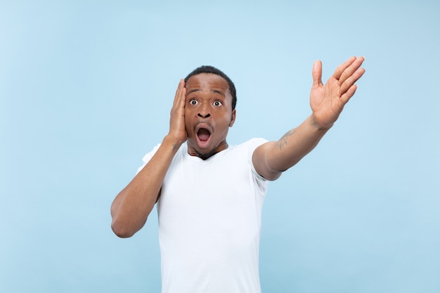 Demi-longueur gros plan portrait de jeune homme afro-américain en chemise blanche sur fond bleu. Émotions humaines, expression faciale, publicité, concept de vente. Pointant, choisissant, étonné. Copyspace.