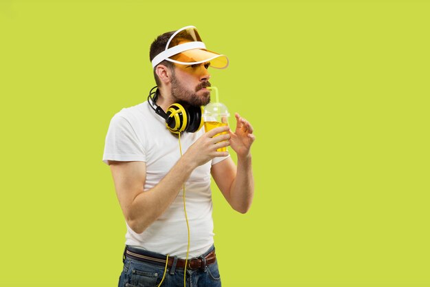 Demi-longueur gros plan portrait de jeune homme en chemise sur l'espace jaune. Modèle masculin avec un casque et une boisson.