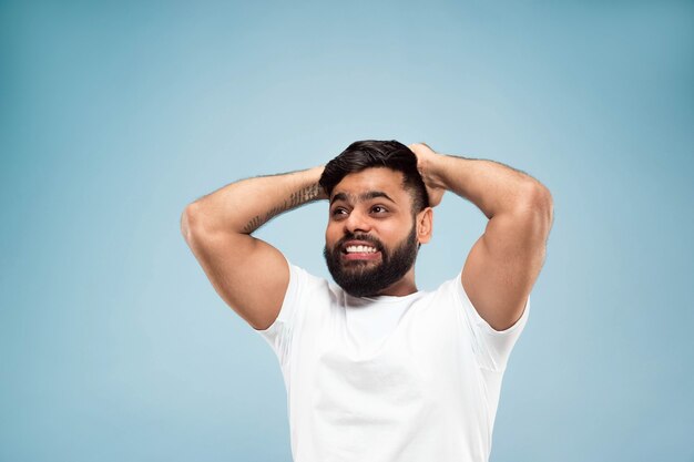 Demi-longueur gros plan portrait de jeune homme hindou en chemise blanche sur fond bleu. Émotions humaines, expression faciale, ventes, concept publicitaire. Espace négatif. Des sentiments heureux choqués, étonnés ou fous.