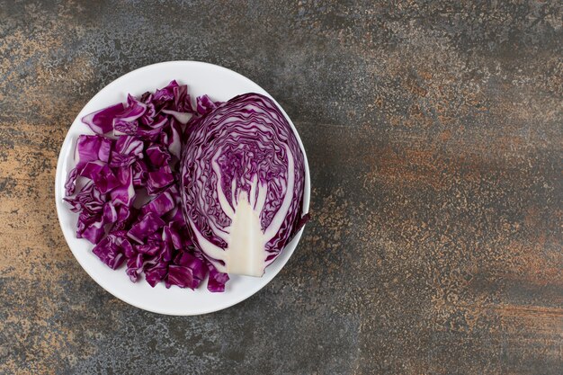 Un demi-morceau de chou rouge à côté de chou finement haché, sur l'assiette, sur la surface en marbre