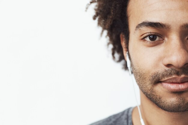 Demi visage bouchent le portrait d'un homme africain heureux dans les écouteurs souriant en écoutant de la musique fumante.