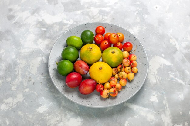 Demi-vue de dessus de composition de fruits mandarines citrons prunes à l'intérieur de la plaque sur un bureau gris clair.