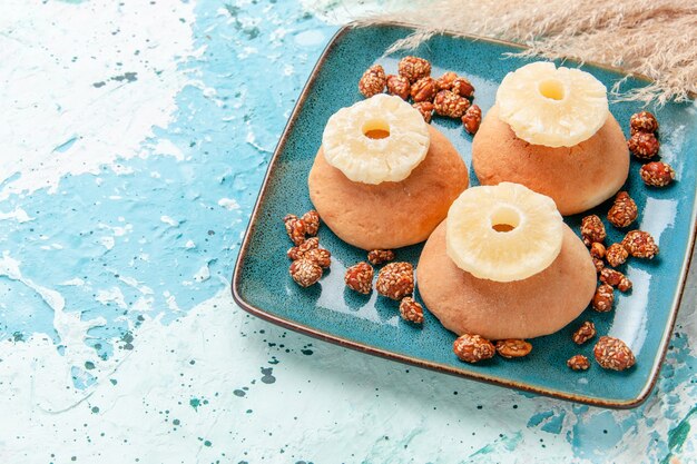 Demi-vue de dessus de délicieux gâteaux avec des anneaux d'ananas séchés et des noix sucrées sur la surface bleu clair cuire le gâteau biscuit noix de sucre sucré