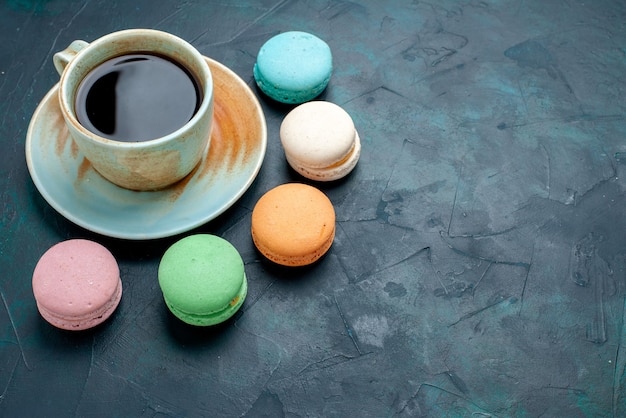 Demi-vue de dessus tasse de thé avec des macarons français sur fond bleu foncé.