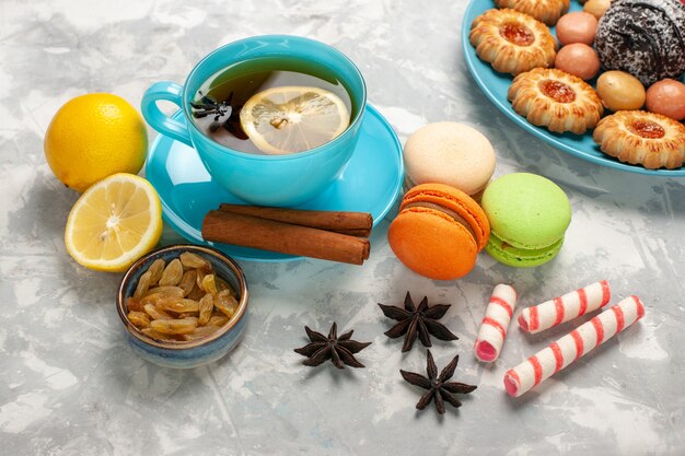 Demi-vue de dessus tasse de thé avec des macarons et des raisins secs sur la surface blanche