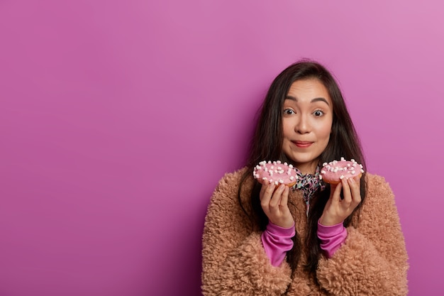 La dent sucrée féminine tient de délicieux beignets colorés glacés, a une dépendance au sucre, veut manger un délicieux dessert en ce moment