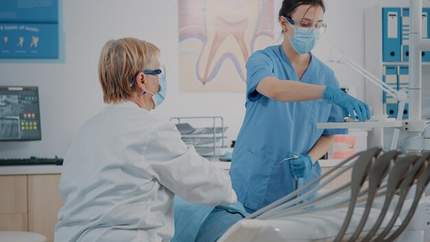 Dentiste et assistant effectuant une procédure de soins bucco-dentaires sur un patient ayant des problèmes de carie. Équipe stomatologique utilisant un instrument de forage pour opérer et faire une extraction dentaire, une procédure de dentisterie.