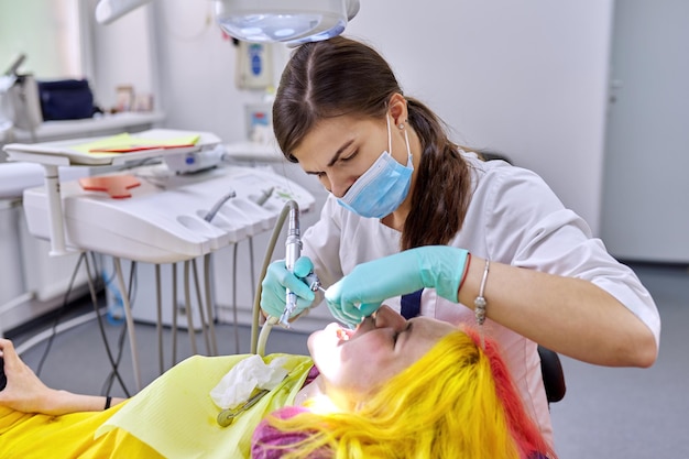 Dentiste femme traitant les dents du patient, jeune femme en fauteuil à la clinique dentaire. vue rapprochée du vrai traitement dentaire d'une adolescente, photographie de reportage