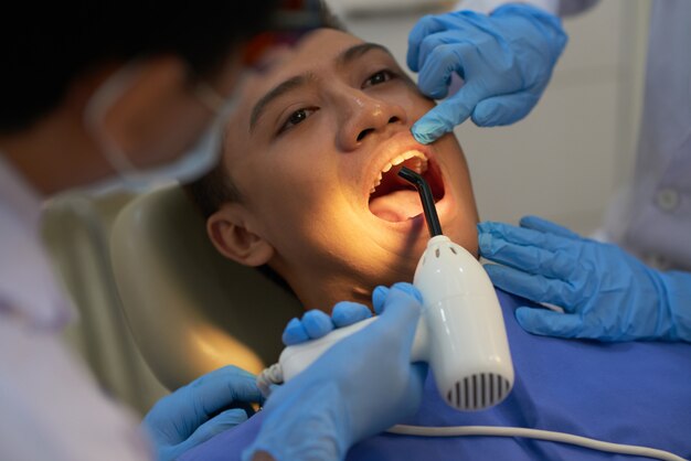 Dentiste guérissant le remplissage des dents d'un patient asiatique avec une lumière ultraviolette