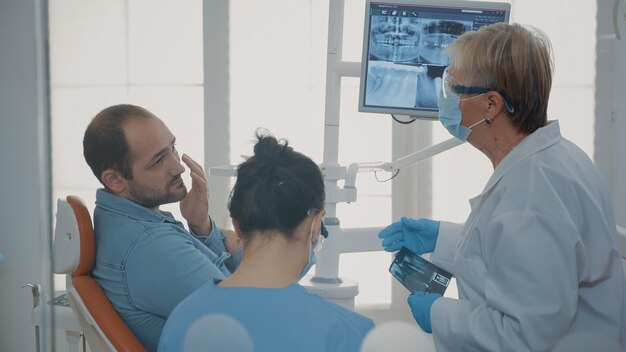 Dentiste et infirmière expliquant la radiographie au patient souffrant de maux de dents dans le cabinet de stomatologie. Équipe de spécialistes faisant une consultation de soins bucco-dentaires pour traiter l'homme souffrant d'un problème de prothèse dentaire.