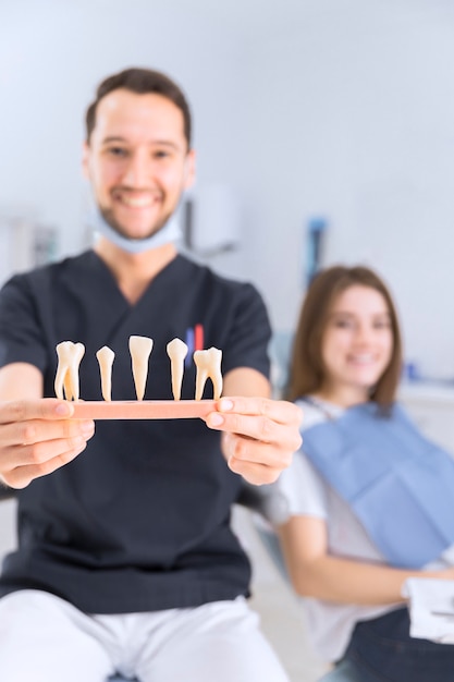 Photo gratuite dentiste mâle montrant le modèle de dents assis devant une patiente