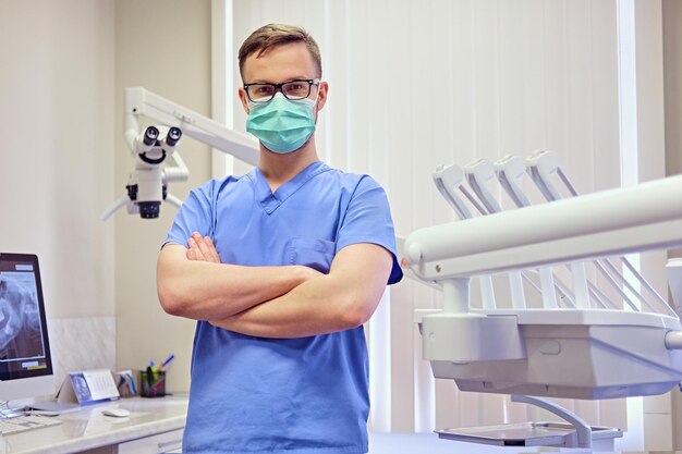 Dentiste masculin dans une pièce avec équipement médical en arrière-plan.