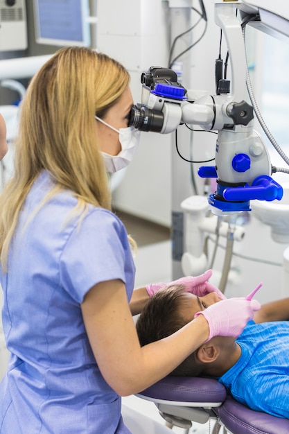 Dentiste regardant les dents du garçon à l&#39;aide d&#39;un microscope dentaire