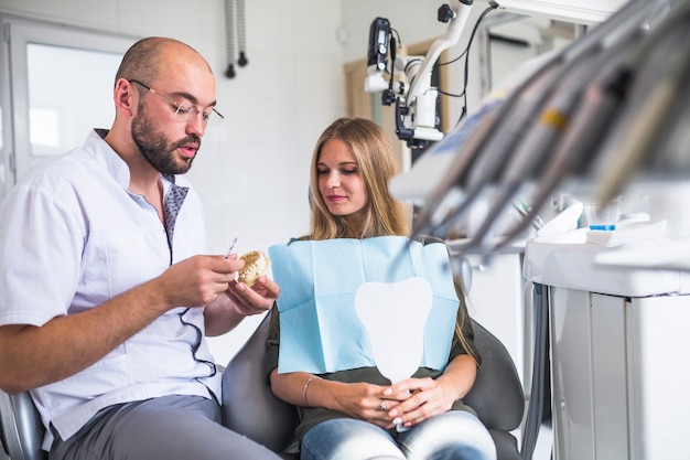 Dentiste travaillant sur la mâchoire dentaire près d&#39;une patiente assise sur un fauteuil dentaire