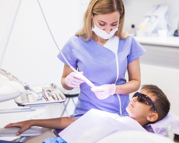 Dentiste utilisant un détartreur à ultrasons pour traiter les dents d&#39;un garçon en clinique