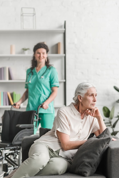 Déprimé jeune femme assise sur le canapé en face de l&#39;infirmière debout avec fauteuil roulant