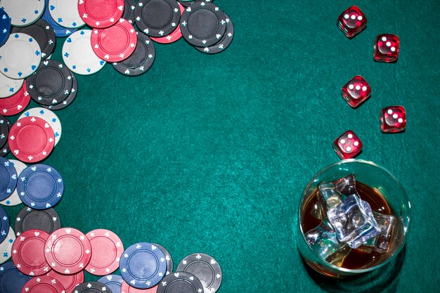 Dés rouges; jetons de casino et verre à whisky avec des glaçons sur la table de poker verte