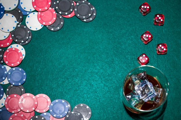 Dés rouges; jetons de casino et verre à whisky avec des glaçons sur la table de poker verte