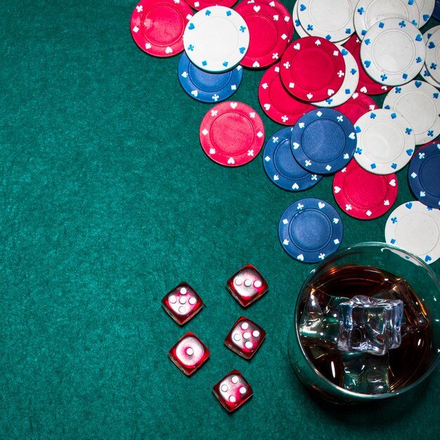 Dés rouges; jetons de casino et verre de whisky sur la table de poker verte