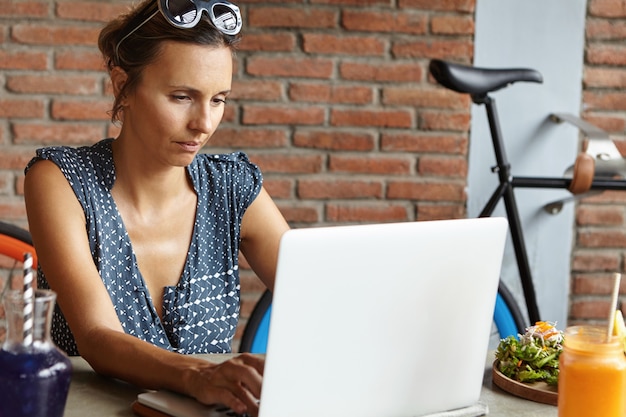 Photo gratuite designer féminin sérieux ou photographe assis à table avec de la nourriture devant un ordinateur portable ouvert