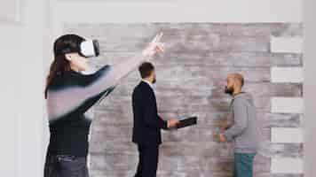 Photo gratuite designer féminine avec des lunettes de réalité virtuelle dans un appartement vide pendant que l'agent immobilier parle avec le propriétaire en arrière-plan.