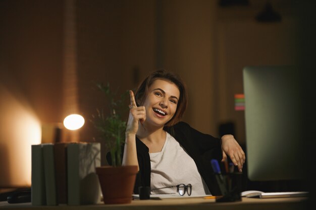 Designer de jeune femme heureuse assis dans le bureau la nuit