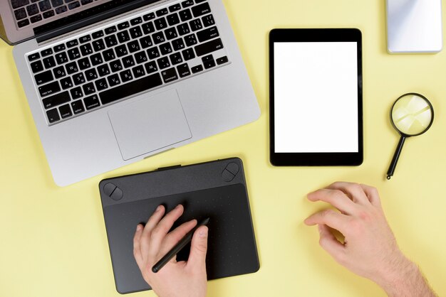 Designer travaillant sur une tablette numérique graphique avec un stylet sur un bureau jaune