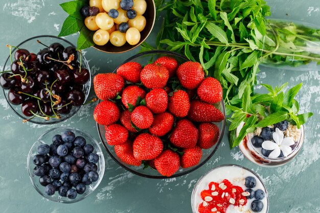 Dessert dans un vase et un gobelet avec fraise, myrtille, menthe, cerise à plat sur une surface en plâtre