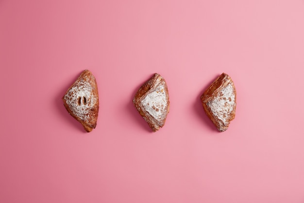 Dessert de pâte feuilletée avec garniture de confiture et sucre en poudre sur fond rose transparent. Cuire des gâteaux sucrés pour les manger. Produits de boulangerie et confiserie. Aliments riches en calories faits maison. Tir aérien