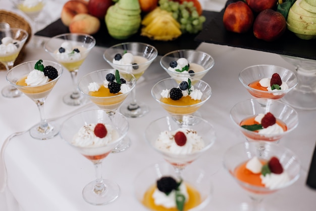 Desserts de gelée colorés avec des baies et de la crème dans la verrerie sur le buffet de banquet