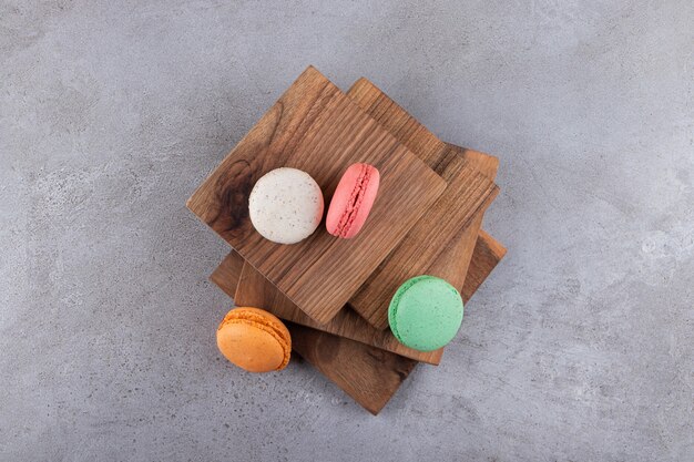 Desserts macarons sucrés colorés placés sur planche de bois.
