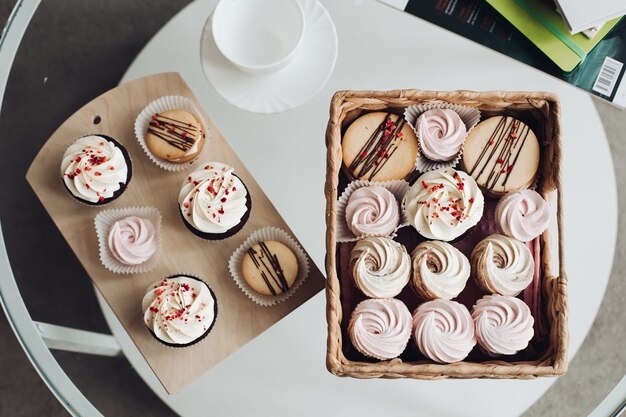 Desserts sur table basse. cupcakes avec garniture crémeuse et crème fouettée dans un panier et une planche en bois avec une tasse et une soucoupe en céramique blanche.