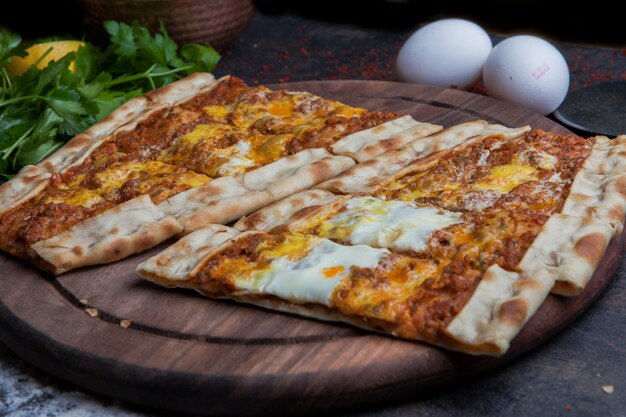 De dessus pide avec de la viande hachée et des œufs et du persil et un couteau à pizza dans un plateau en bois