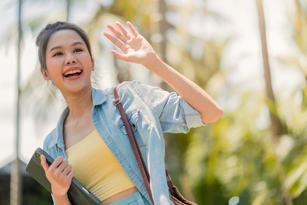 Détendez-vous décontracté insouciant souriant asiatique femme nomade numérique programmeur indépendant main tenir un ordinateur portable marchant à la plage et cocotier bleu ciel nouveau style de vie millénaire travaillant n'importe où avec bonheur