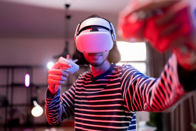 Détendez-vous un homme adulte asiatique portant un casque de réalité virtuelle et tenant des contrôleurs Joue dans un jeu vidéo de sport de boxe à la maison Jouant à un jeu de sport actif VR en ligne dans le salon avec une ambiance d'éclairage RVB